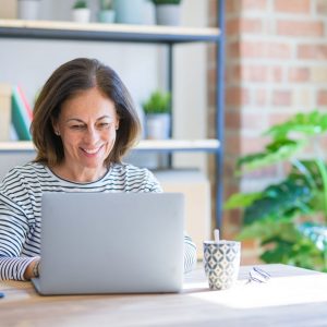 Woman at computer working to get clients online. She is smiling because she has found her ideal clients after listening to A Profitable Impact.